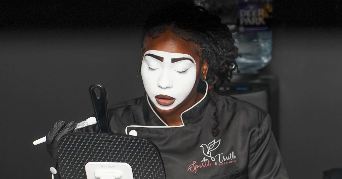 A performing artist in white mime makeup, mid-performance